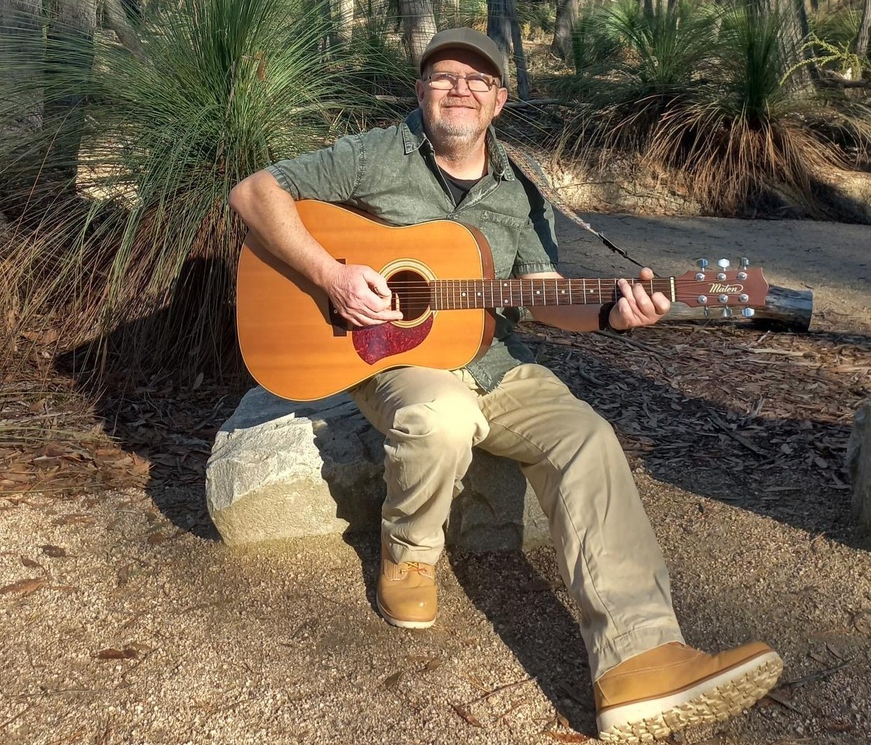 Gerry sitting on a rock playing a guitar